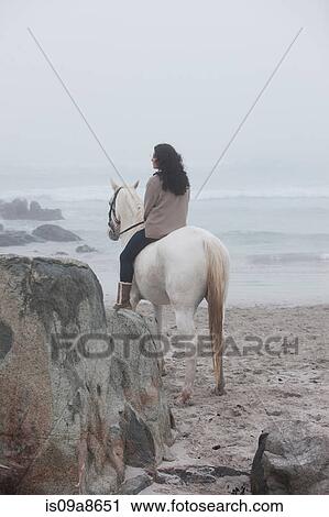 Stock Image - Woman riding horse on beach. Fotosearch