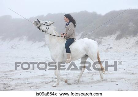Stock Photo - Woman riding horse on beach. Fotosearch
