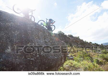 Stock Image - Young couple carrying mountain bikes down from rocks. Fotosearch