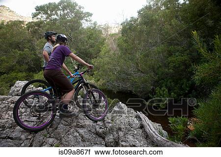 Young couple on mountain bikes on edge of rock View Large Photo Image Stock Image - Young couple on mountain bikes on edge of rock. Fotosearch