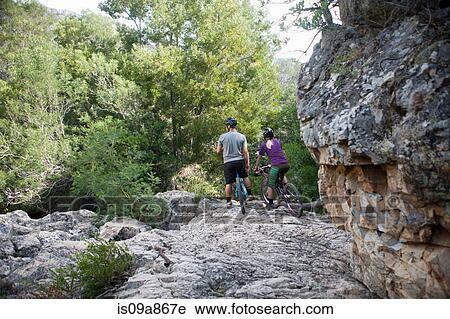 Stock Image - Young couple resting on mountain bikes on rock. Fotosearch