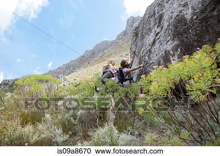 Stock Image - Young hikers examining large boulder. Fotosearch