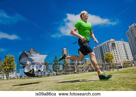 Stock Image - Young man jogging in city park with parachute. Fotosearch