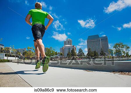 Stock Photo - Young man jogging in city, rear view. Fotosearch