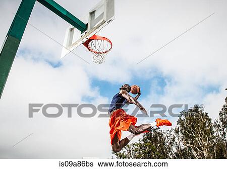 Stock Photograph - Young man jumping to score hoop in basketball. Fotosearch
