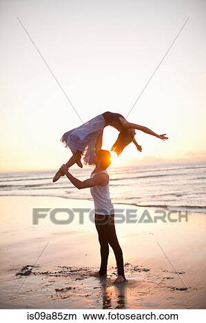 Picture - Young man lifting dancing partner on sunlit beach. Fotosearch