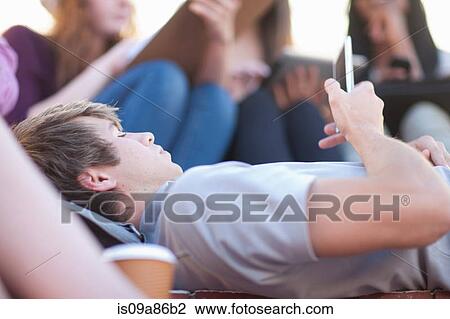 Young man lying down using smartphone View Large Photo Image Stock Image - Young man lying down using smartphone. Fotosearch