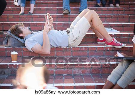 Young man lying on steps using smartphone View Large Photo Image Stock Photo - Young man lying on steps using smartphone. Fotosearch