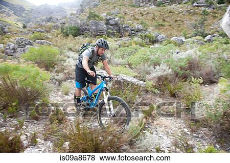 Stock Photo - Young man mountain biking through scrubland. Fotosearch