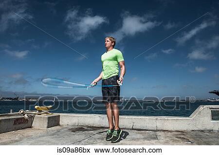 Stock Photo - Young man using skipping rope on pier. Fotosearch