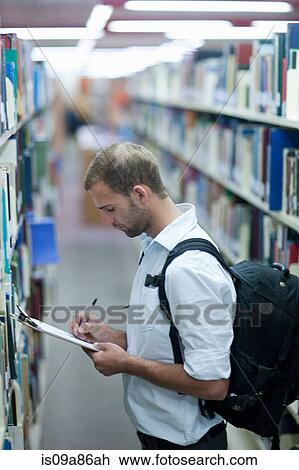 Young man writing on clipboard in library View Large Photo Image Stock Image - Young man writing on clipboard in library. Fotosearch