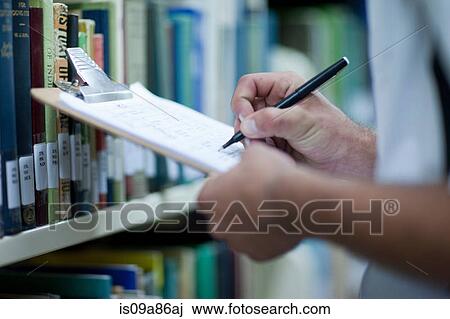 Young man writing on clipboard in library View Large Photo Image Stock Image - Young man writing on clipboard in library. Fotosearch