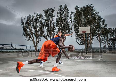 Stock Image - Young men playing basketball on court. Fotosearch