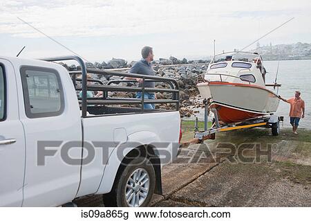 Stock Image - Young men with motorboat and trailer in harbor. Fotosearch