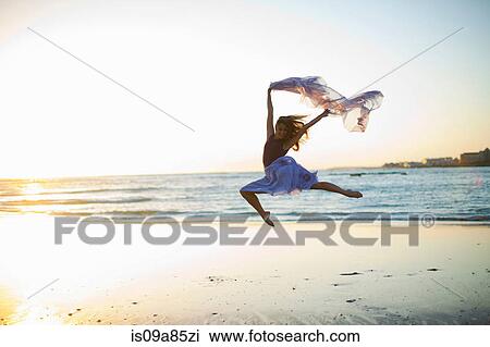 Stock Image - Young woman dancing on sunlit beach. Fotosearch