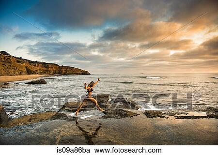 Young woman in bikini leaping from rocks on beach View Large Photo Image Stock Image - Young woman in bikini leaping from rocks on beach. Fotosearch