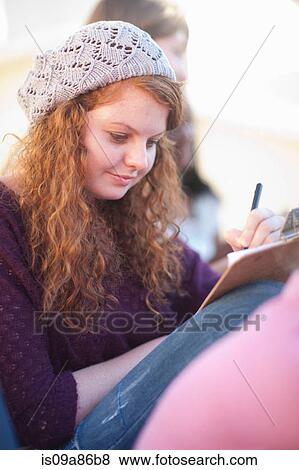 Stock Photo - Young woman wearing knit hat writing on clipboard. Fotosearch
