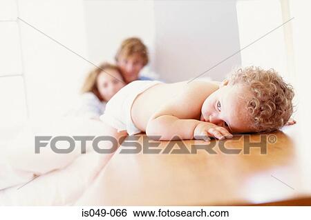 Baby resting with parents in the background View Large Photo Image Stock Photograph - Baby resting with parents in the background. Fotosearch