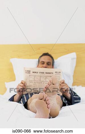 Stock Photograph - Man reading newspaper in bed. Fotosearch
