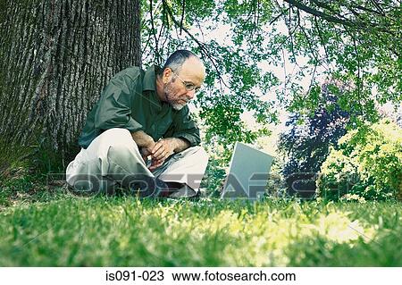 Man looking at laptop in park View Large Photo Image Stock Image - Man looking at laptop in park. Fotosearch