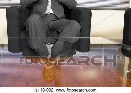 Stock Image - Businessman reflected in glass table. Fotosearch