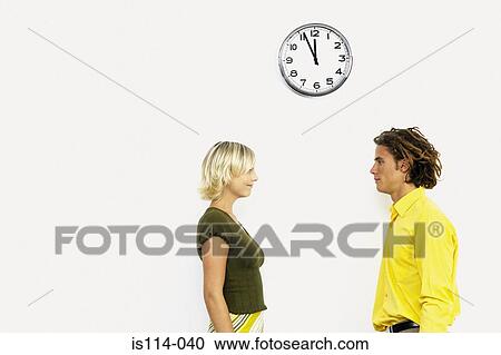 Stock Image - Businessman and businesswoman underneath wall clock. Fotosearch