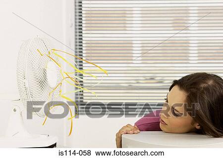 Stock Photo - Businesswoman cooled by fan in office. Fotosearch