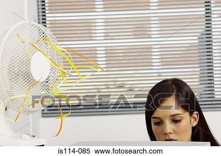 Businesswoman cooled by fan in office View Large Photo Image Stock Photography - Businesswoman cooled by fan in office. Fotosearch
