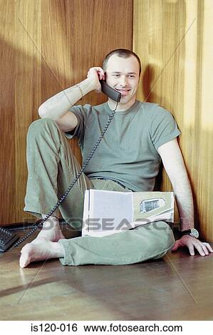 Stock Photograph - Man on telephone sitting on floor. Fotosearch