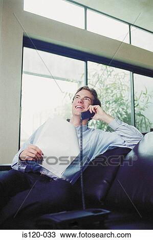 Stock Image - Man sitting on sofa with telephone. Fotosearch