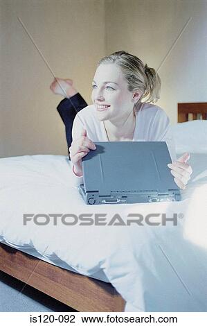 Stock Image - Woman in bedroom with laptop. Fotosearch