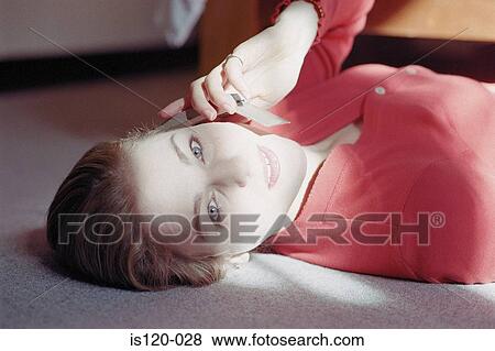 Stock Photo - Woman lying on carpeted floor with cellphone. Fotosearch