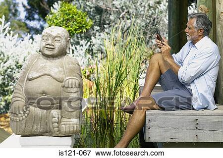 Stock Photo - Man beside pool and buddha with cellphone. Fotosearch