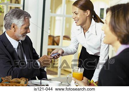 Picture - Waitress handing cellphone to businessman. Fotosearch