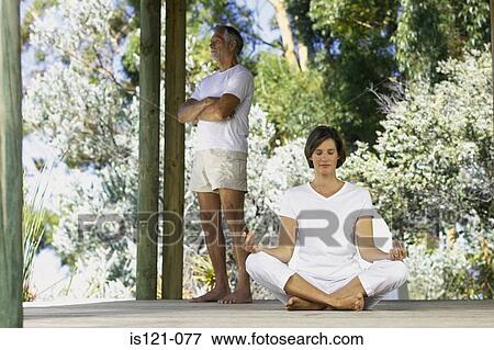 Stock Photo - Woman doing yoga outside with man standing. Fotosearch