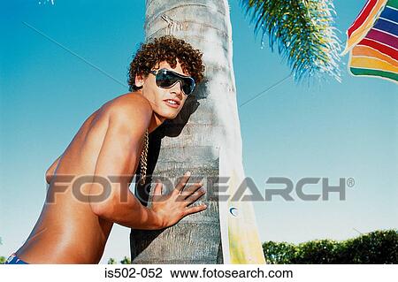 Stock Image - Young man leaning against a palm tree. Fotosearch