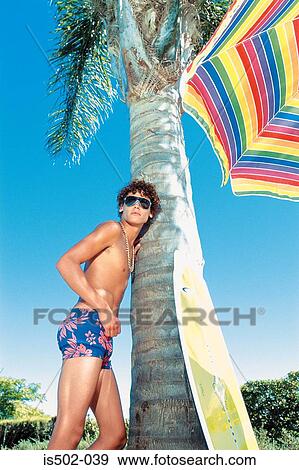 Young man leaning against a palm tree View Large Photo Image Stock Photo - Young man leaning against a palm tree. Fotosearch