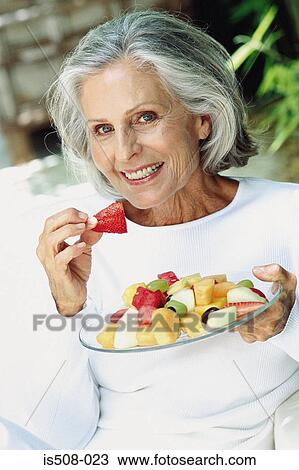 Stock Image - Ageing woman eating outdoors. Fotosearch