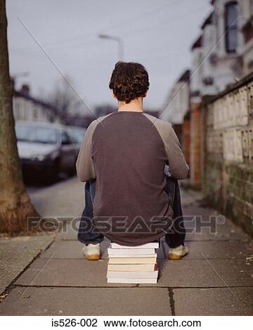 Stock Image - A young man sitting on a pile of books. Fotosearch