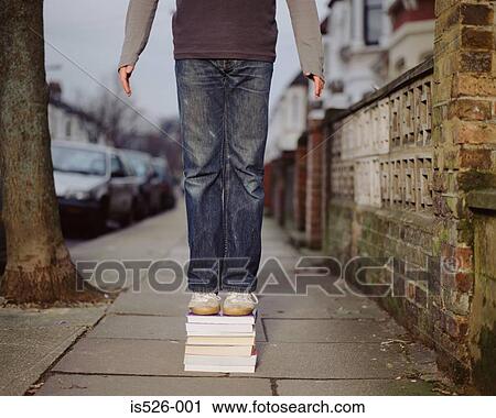 Stock Image - A young man standing on a pile of books. Fotosearch