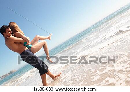 Man holding a woman on a beach View Large Photo Image Stock Image - Man holding a woman on a beach. Fotosearch