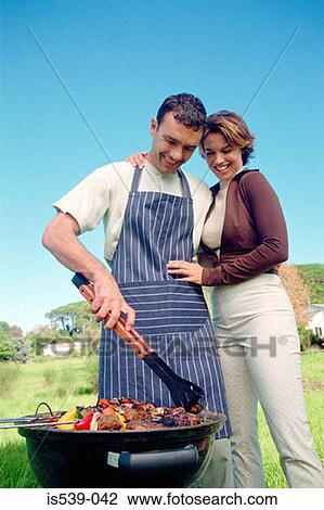 Stock Image - Couple cooking food on barbeque. Fotosearch