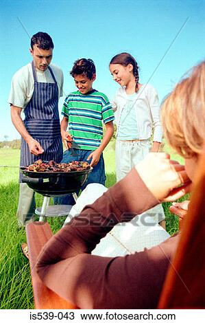 Stock Image - Family cooking food on barbeque. Fotosearch