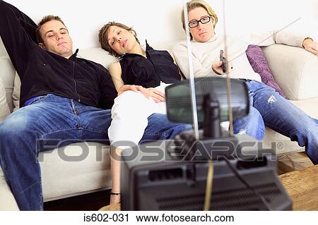 Stock Image - Friends watching television on sofa. Fotosearch