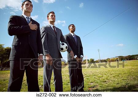 Stock Image - Businessmen standing in row in field. Fotosearch