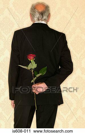 Stock Image - Senior man hiding red rose. Fotosearch