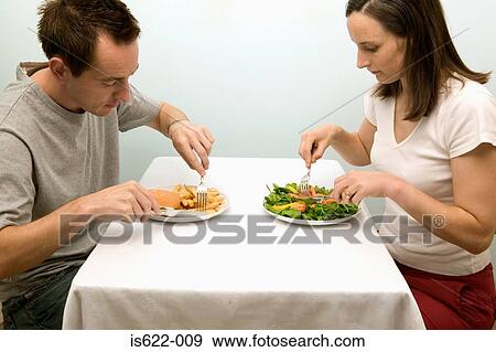 Couple eating contrasting meals View Large Photo Image Stock Photo - Couple eating contrasting meals. Fotosearch