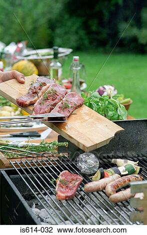 Stock Image - Putting steaks on barbeque.. Fotosearch
