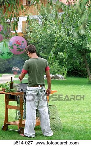 Stock Photo - Young male cooks on barbeque. Fotosearch