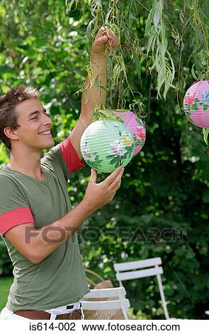 Stock Image - Young male hanging lampshade.. Fotosearch